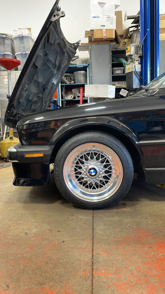 BMW vehicle with open hood in auto repair shop, showcasing detailed wheel and tire, emphasizing expert diagnostics and service.