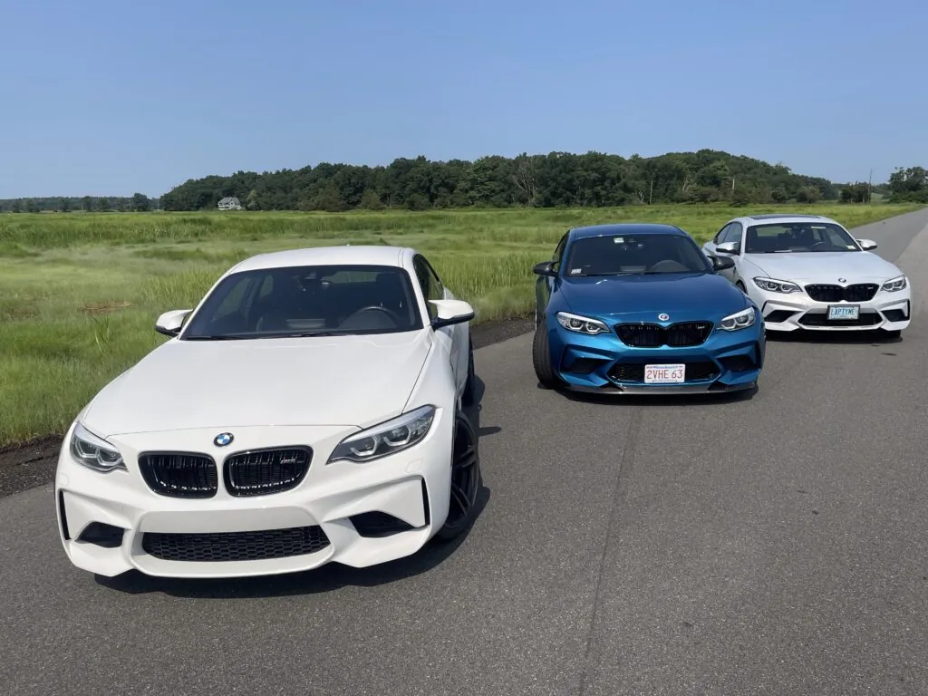 Three BMW M2 models in a row, showcasing a white, blue, and silver car on a scenic road, emphasizing Schneller BMW's expertise in BMW vehicle service and performance.
