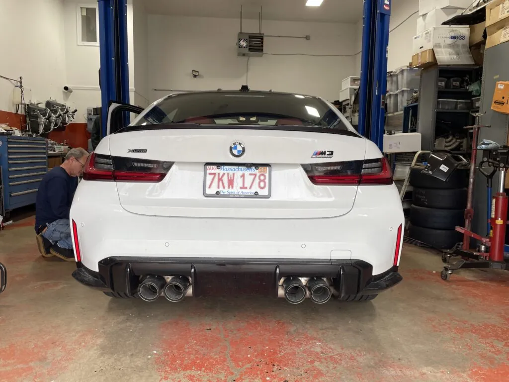 BMW M3 in service bay with technician inspecting vehicle, showcasing diagnostic tools and equipment for check engine light issues.