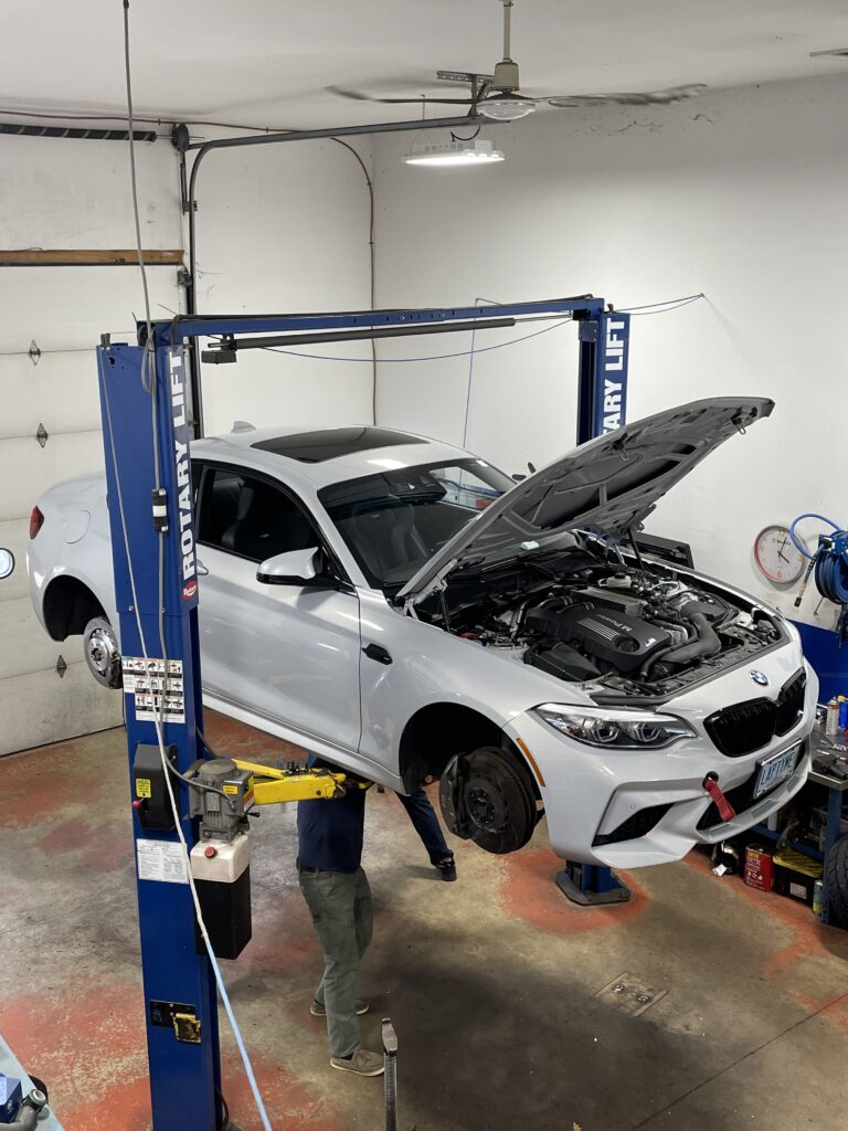 BMW vehicle on a hydraulic lift in a service garage, technician inspecting engine under the hood, emphasizing professional diagnostic services for check engine light issues.