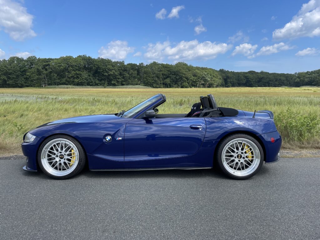 BMW Z4 convertible parked on a scenic road, showcasing its sleek blue exterior and alloy wheels, surrounded by green fields and a clear sky, emphasizing Schneller BMW's focus on performance and quality service for BMW enthusiasts.